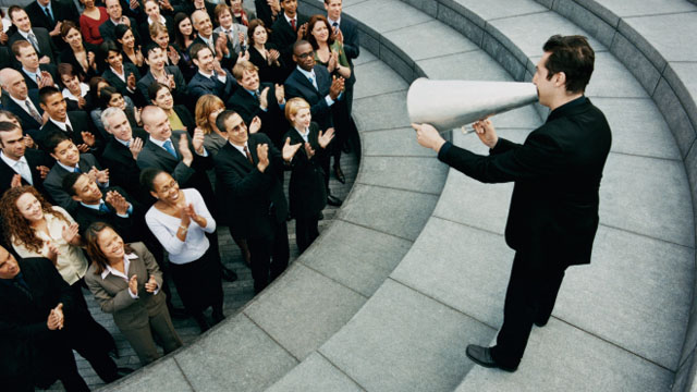 Businessman Standing on Steps Outside Talking Through a Megaphone, Large Group of Business People Listening and Applauding
